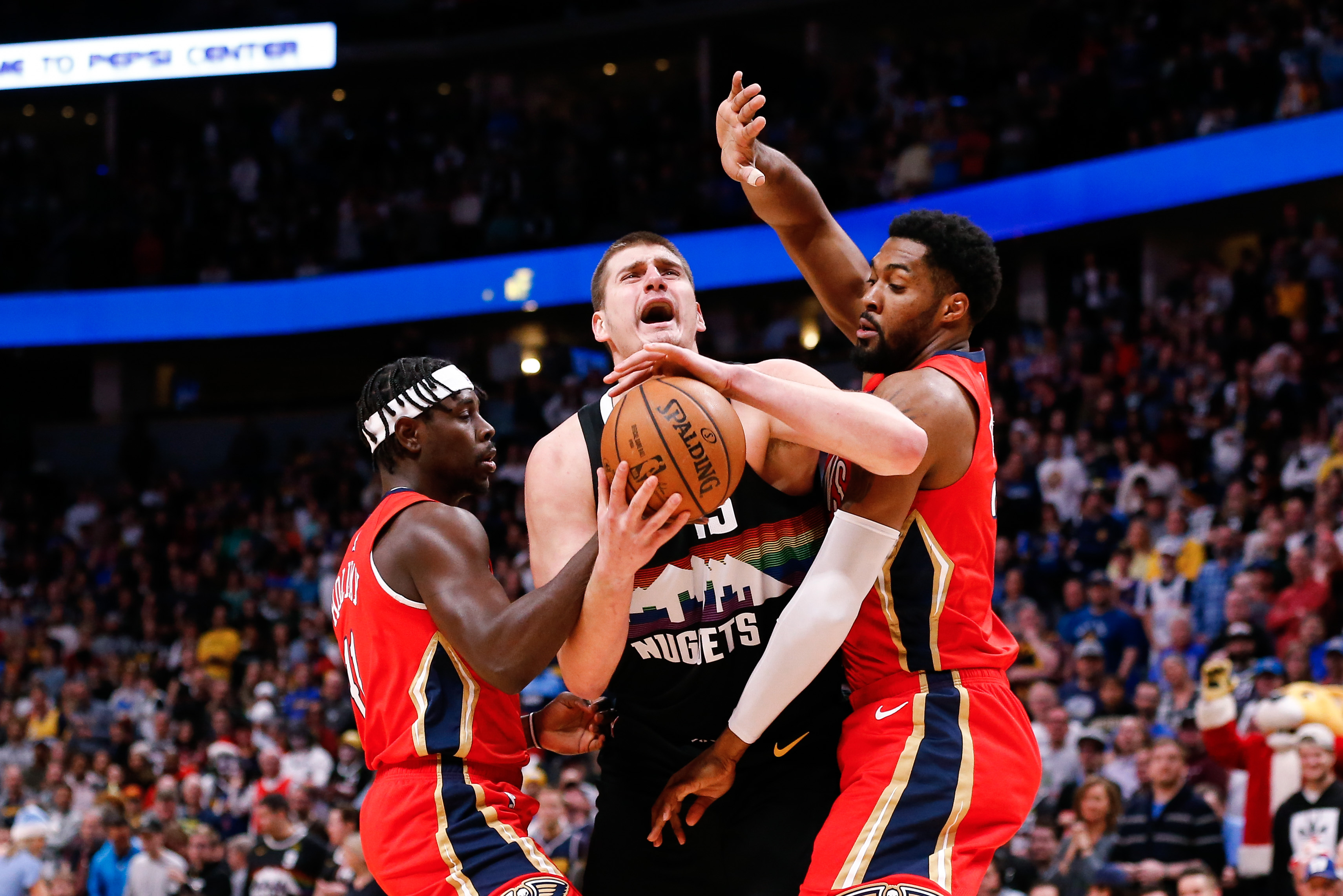 Denver Nuggets center Nikola Jokic (15) is fouled by New Orleans Pelicans guard Jrue Holiday (11) and forward Derrick Favors (22) in the first quarter at the Pepsi Center.
