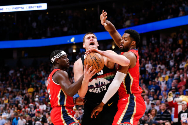 Denver Nuggets center Nikola Jokic (15) is fouled by New Orleans Pelicans guard Jrue Holiday (11) and forward Derrick Favors (22) in the first quarter at the Pepsi Center.