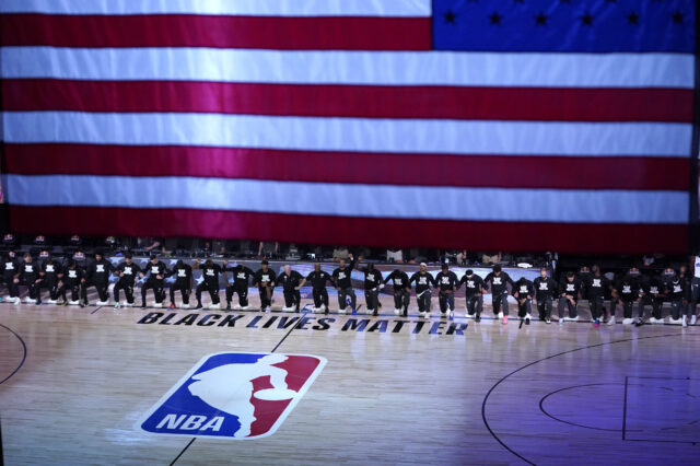 Members of the Orlando Magic and Brooklyn Nets kneel around a Black Lives Matter logo during the national anthem before the start of an NBA basketball game.
