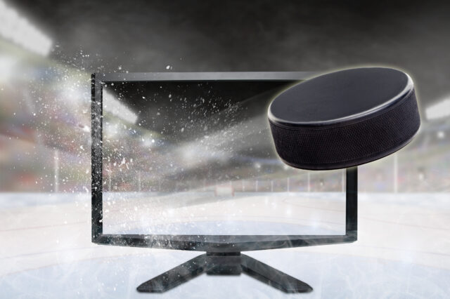 Hockey puck flying out of shattering TV screen in stadium with copy space. Concept of realistic 3D or 4D sports TV, virtual reality VR or computer gaming. Photos of hockey puck and monitor taken separately and then composited onto fictitious stadium created in Photoshop.