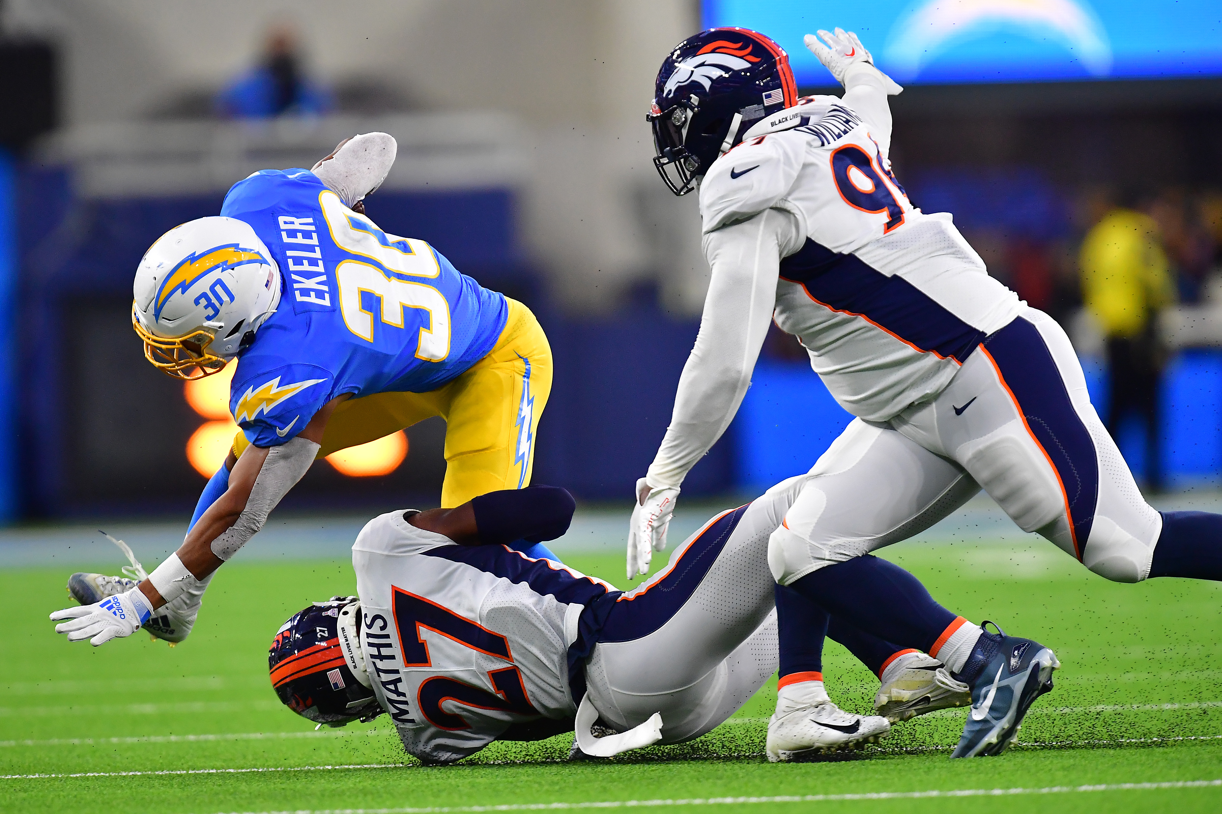 Los Angeles Chargers running back Austin Ekeler (30) is brought down by Denver Broncos cornerback Damarri Mathis (27) and Denver Broncos defensive tackle DeShawn Williams (99) during the first half at SoFi Stadium.