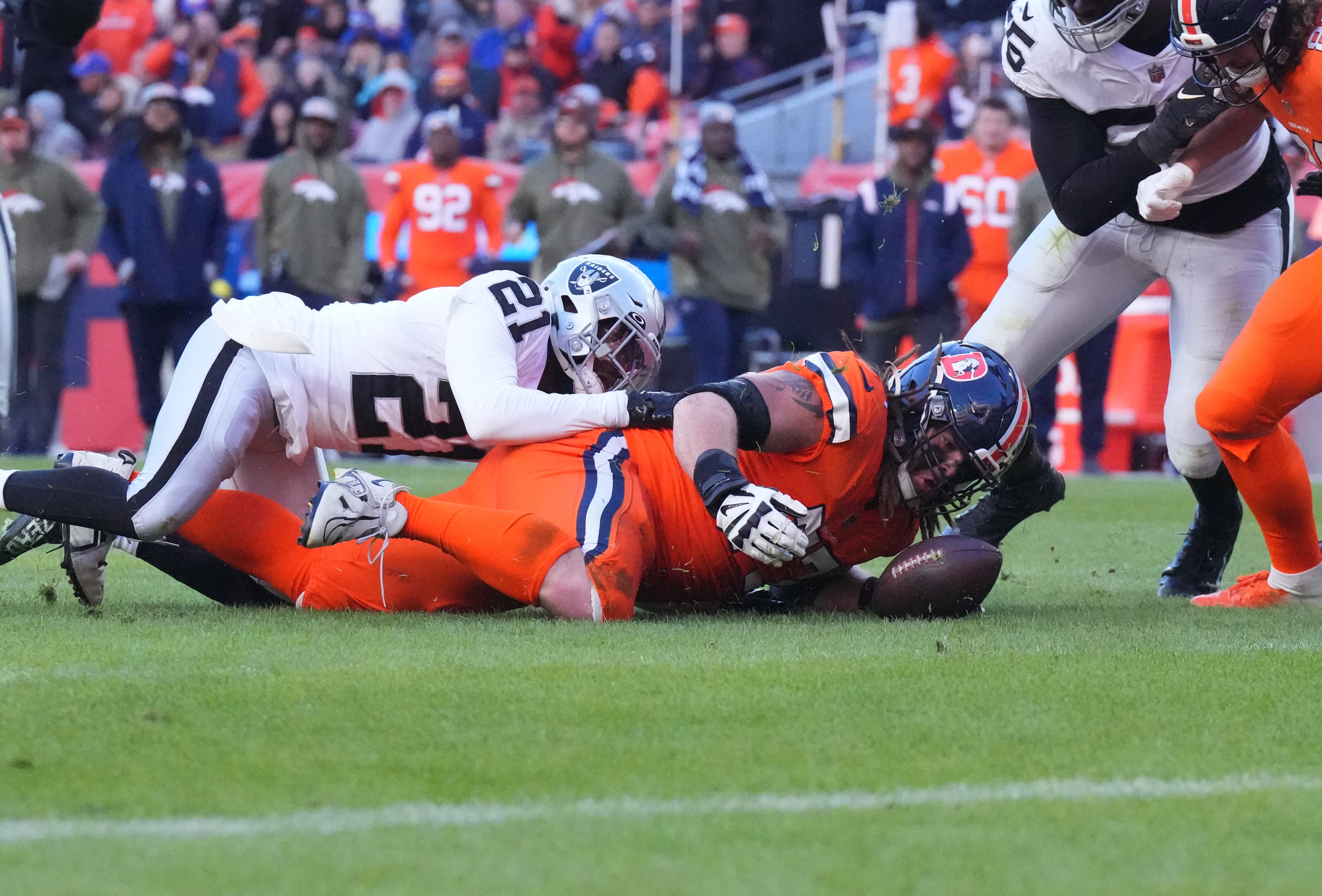 Las Vegas Raiders cornerback Amik Robertson (21) and Denver Broncos guard Quinn Meinerz (77) reach for a fumbled football in the second quarter at Empower Field at Mile High. 
