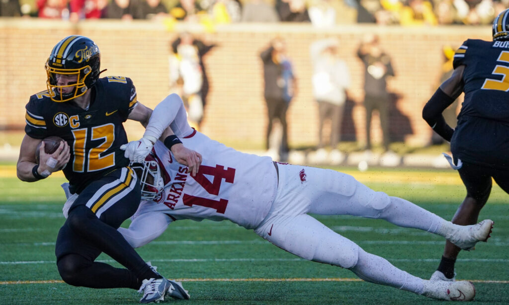 Missouri Tigers quarterback Brady Cook (12) is tackled by Arkansas Razorbacks defensive lineman Jordan Domineck (14) during the first half at Faurot Field at Memorial Stadium. (Coach Prime)