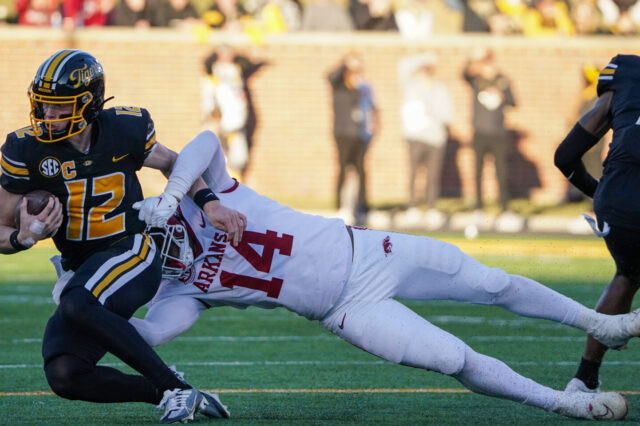 Missouri Tigers quarterback Brady Cook (12) is tackled by Arkansas Razorbacks defensive lineman Jordan Domineck (14) during the first half at Faurot Field at Memorial Stadium. (Coach Prime)
